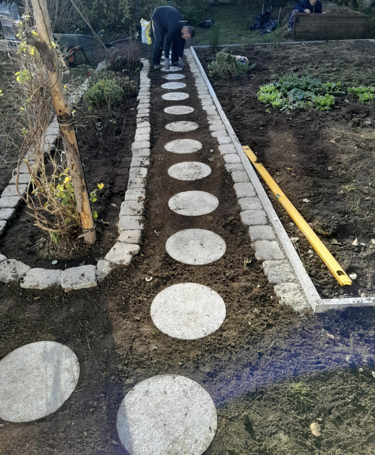 Trittsteinweg aus runden Granitplatten mit Natursteinpflaster-Einfassung im Gartenbeet